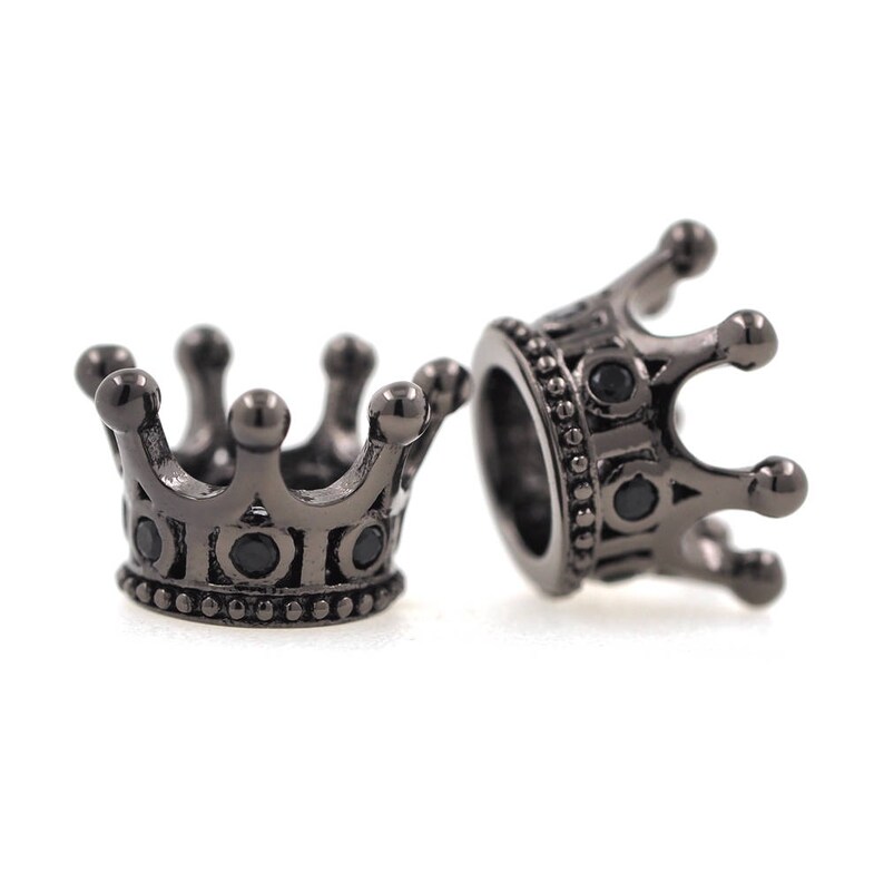 May include: Two black metal crown-shaped beads with black gemstones. The beads are designed to be used for jewelry making.
