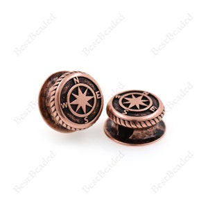 May include: Two copper-colored compass charm beads with a rope design around the edge. The compass features a star with the letters N, S, E, and W.