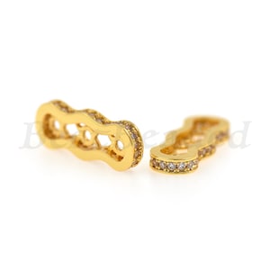 May include: Two gold-toned connector pieces for jewelry making. Each piece has a wavy design with clear rhinestones around the edge.