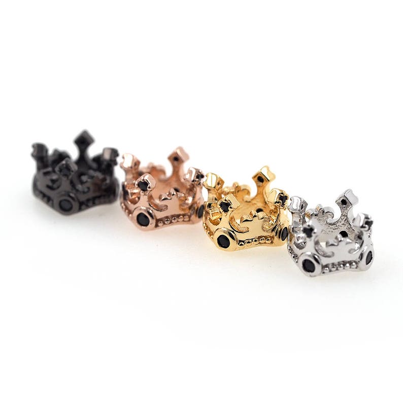 May include: Four small crown-shaped charms with black cubic zirconia stones. The crowns are in black, rose gold, gold, and silver.
