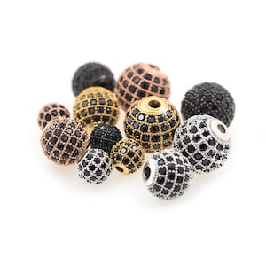 May include: Assortment of black, gold, and silver round beads with a sparkly finish. The beads are made of metal and have a variety of sizes.