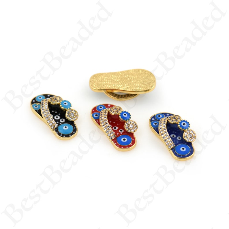 May include: Four gold-tone flip-flop charms with blue evil eye details and clear rhinestones. The flip-flops are in black, red, blue, and gold.