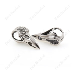 May include: Two silver metal bird skull beads with intricate details. The beads have a hollow design and are perfect for jewelry making or crafting.