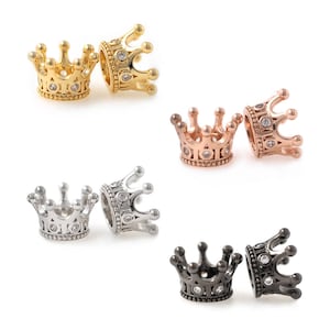 May include: Six crown-shaped charms in different metal finishes: gold, rose gold, silver, and black. Each charm features a detailed crown design with clear rhinestones.