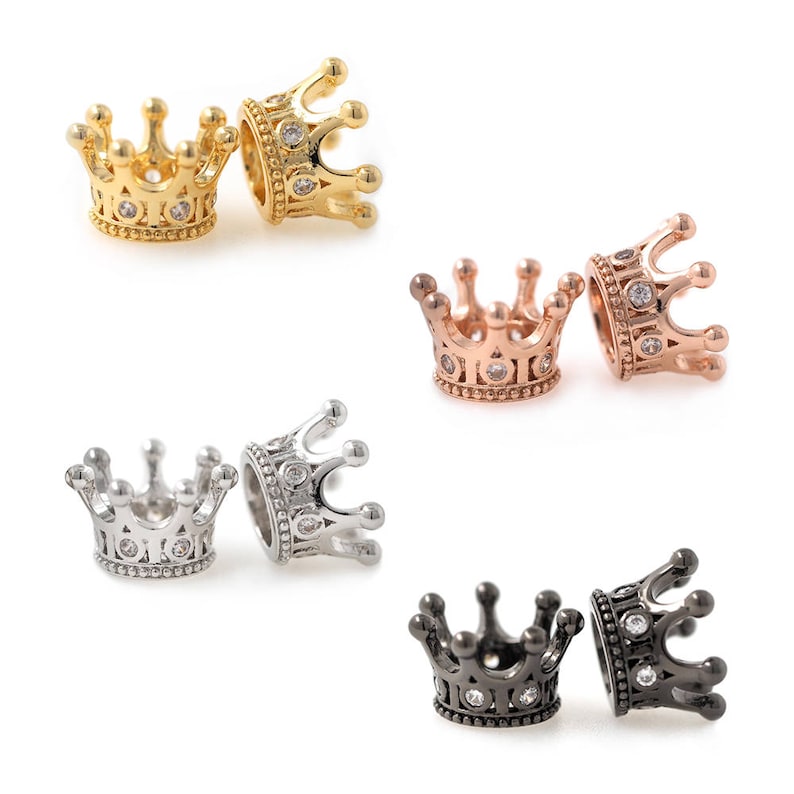 May include: Six crown-shaped charms in different metal finishes: gold, rose gold, silver, and black. Each charm features a detailed crown design with clear rhinestones.