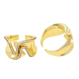 Op de afbeelding: Twee goudkleurige ringen met een golvend ontwerp. Eén ring is open en beide zijn versierd met kleine, sprankelende steentjes langs de randen. De ringen hebben een gepolijste afwerking en staan tegen een witte achtergrond.