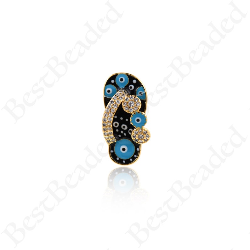 May include: Gold-tone charm featuring a black flip-flop with blue evil eye details and clear rhinestones.