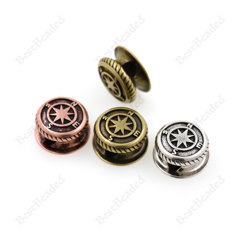 May include: Three compass-shaped metal toggles in different finishes: antique copper, antique brass, and silver. Each toggle features a compass rose with the letters N, S, E, and W around the star.