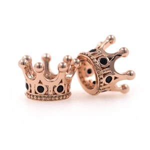 May include: Two gold-tone crown-shaped bead charms with black accents. The charms are designed to be used on a bracelet or necklace.