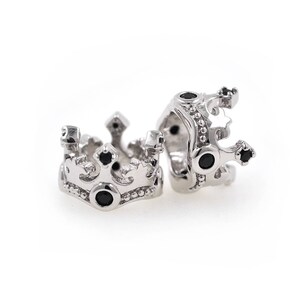 May include: Two silver crown-shaped charms with black gemstones. The charms are detailed with intricate designs and are perfect for adding a touch of royalty to jewelry.