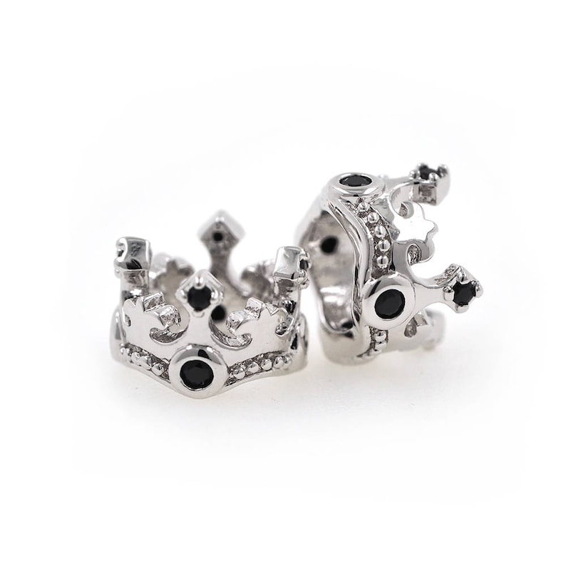May include: Two silver crown-shaped charms with black gemstones. The charms are detailed with intricate designs and are perfect for adding a touch of royalty to jewelry.