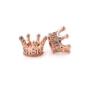 May include: Two gold-tone crown-shaped charms with clear cubic zirconia stones.
