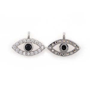 May include: Two silver evil eye charms featuring clear and black cubic zirconia stones. The charms are shaped like an eye with a small loop at the top for attaching to a necklace or bracelet.