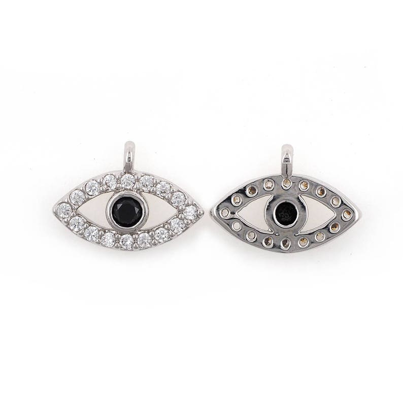 May include: Two silver evil eye charms featuring clear and black cubic zirconia stones. The charms are shaped like an eye with a small loop at the top for attaching to a necklace or bracelet.