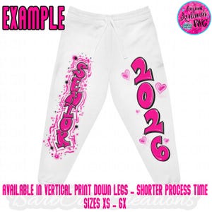 May include: White sweatpants with a drawstring waist, featuring pink airbrushed text that reads "SENIOR" and "2026" with heart accents. The word "EXAMPLE" is at the top. The text "AVAILABLE IN VERTICAL PRINT DOWN LEGS - SHORTER PROCESS TIME SIZES XS - 6X" is at the bottom.