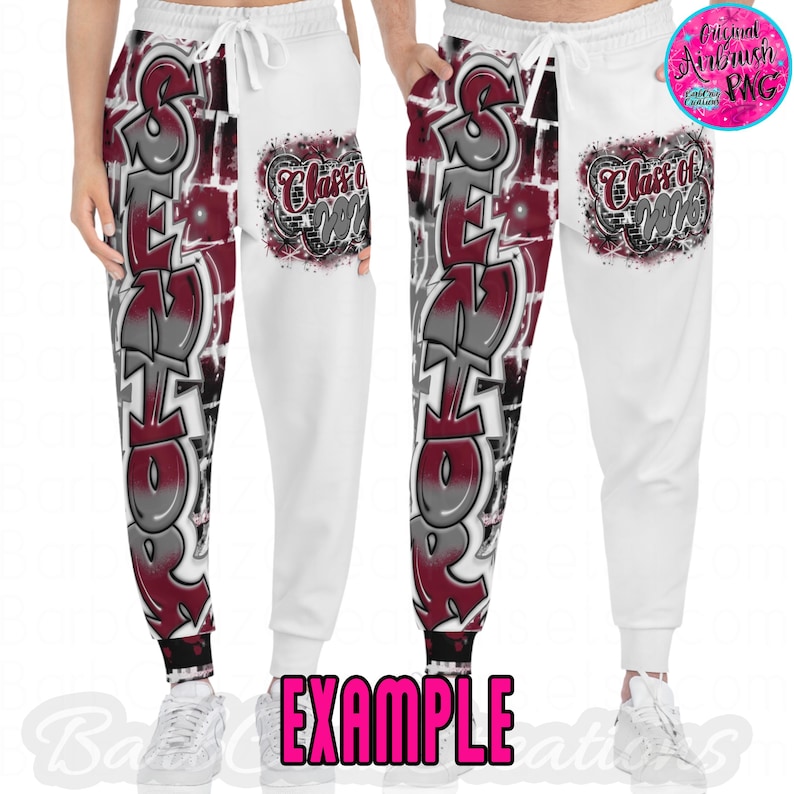 Peut inclure: Pantalon de surv&ecirc;tement blanc avec taille &eacute;lastique et cordon de serrage, orn&eacute; d'un motif graffiti. Le motif pr&eacute;sente le mot "SENIOR" en gris et bordeaux, avec "Class of 2023" sur la poche. Le mot "EXAMPLE" est imprim&eacute; en bas.
