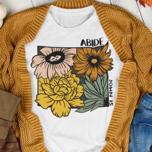 May include: White t-shirt with a floral design and the text "ABIDE JOHN 15" printed on it.