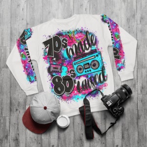 May include: White sweatshirt with a colorful graphic print featuring the text "70's made 80's raised" and a retro boombox and cassette tape.