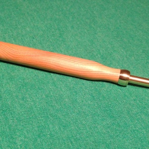 Peut inclure: Un crochet en bois avec une poignée ronde en bois et un crochet en métal. Le crochet est brun clair et la poignée est brun foncé.