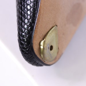 Puede incluir: Primer plano de un bolso de cuero negro con una base de metal dorado. La base tiene un peque&ntilde;o agujero en el centro.