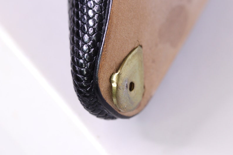 Puede incluir: Primer plano de un bolso de cuero negro con una base de metal dorado. La base tiene un peque&ntilde;o agujero en el centro.