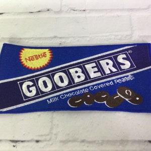 May include: Blue and white embroidered patch with the words "Nestle Goobers Milk Chocolate Covered Peanuts" and a depiction of chocolate covered peanuts.