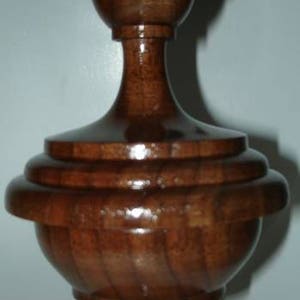 May include: A dark brown wooden finial with a rounded top and a fluted base. The finial has a smooth, polished finish.