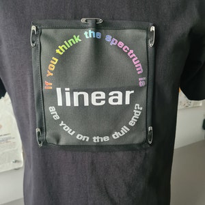 Könnte beinhalten: Schwarzes T-Shirt mit einem regenbogenfarbenen Patch, auf dem steht: "Wenn du denkst, dass das Spektrum linear ist, bist du am langweiligen Ende?"