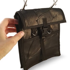 May include: A black leather crossbody bag with a flap closure and a buckle. The bag has two metal clips on the top and a black strap.