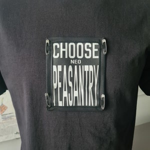 May include: Black t-shirt with a black and white patch that says "CHOOSE NEO PEASANTRY" with safety pins on the edges.