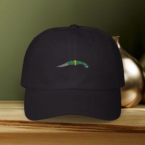 May include: A black baseball cap with an embroidered green and yellow dagger design.