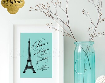 Puede incluir: Un marco rectangular blanco que contiene una impresión azul claro con una silueta negra de la Torre Eiffel y el texto: Paris is always a good idea. Audrey Hepburn. Junto al marco hay una botella de vidrio azul claro con ramas.