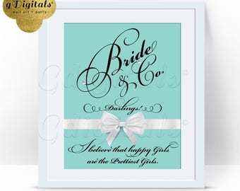 May include: A framed print featuring a light blue background with black cursive text that reads Bride & Co. Darlings! I believe that happy Girls are the Prettiest Girls. A white ribbon with a bow is centered horizontally across the print.