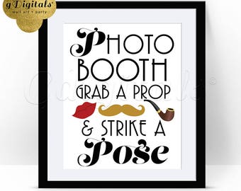 May include: A framed sign with a white background and black text that reads Photo Booth Grab a Prop & Strike a Pose. The design includes a red pair of lips, a gold mustache, and a brown smoking pipe illustration centered on the white surface.