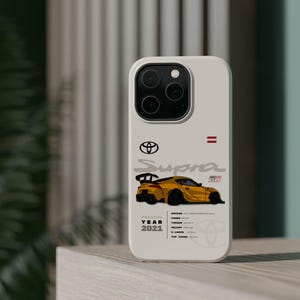Op de afbeelding: Een witte telefoonhoes met een gele sportwagen illustratie, de tekst "Supra GR" en "Year 2021." De hoes bevat ook het Toyota-logo en autospecificaties.