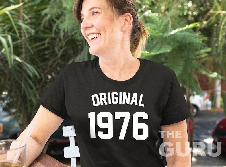 May include: A black t-shirt with white text that reads "ORIGINAL 1976" and "THE GURU" on the bottom right corner.