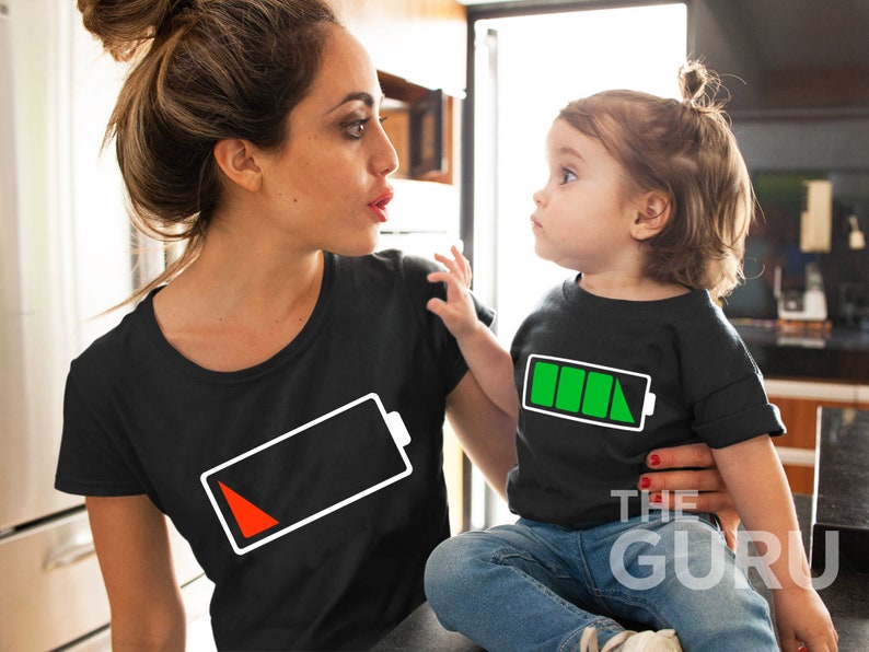 May include: A woman and a child wearing matching black t-shirts with white battery icons. The woman's battery icon is red, indicating low battery, while the child's battery icon is green, indicating full battery.