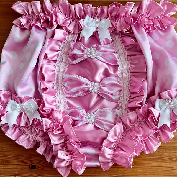 May include: Pink satin baby doll with white polka dots and white satin bows. The baby doll has a ruffled trim and is made of soft, silky fabric.