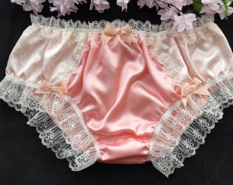 May include: Pink satin underwear with white lace trim and bows. The underwear has a ruffled edge and is made of a soft, silky fabric.
