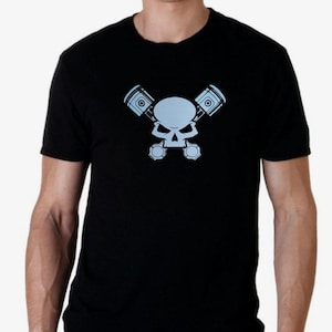 Könnte beinhalten: Schwarzes Kurzarm-T-Shirt mit einem hellblauen Schädel-Design mit gekreuzten Kolben. Die Grafik ist auf der Brust zentriert. Das Shirt besteht aus einem weichen, bequemen Material.