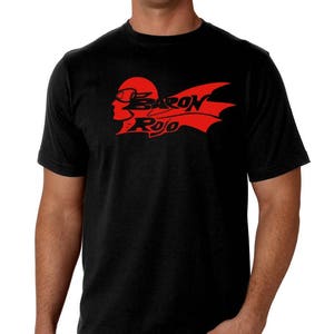 May include: Black t-shirt featuring a red graphic of a profile wearing goggles and a winged design, with the text "BARON ROJO". The shirt is short-sleeved and made of a soft material.