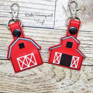 May include: Two red barn-shaped keychains with white trim and black doors. Each keychain has a silver metal clasp and a black button.