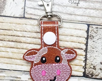 May include: Brown and pink cow keychain with white spots. The keychain has a silver metal clasp and a brown leather strap. Delta Sewing and Vinyl is printed on the top of the image.
