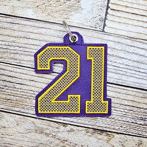 May include: Purple and yellow embroidered keychain with the number 21.