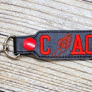 May include: Black leather keychain with a red running figure and the word "COACH" embroidered in red.