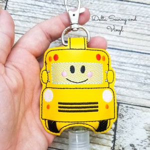 May include: Yellow school bus-shaped hand sanitizer holder with a smiling face, black stitching, and a silver clip.  Delta Sewing and Vinyl.