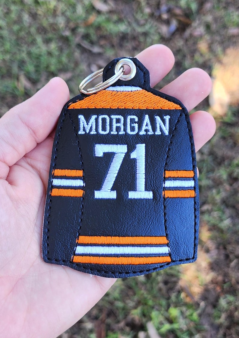 Pu&ograve; includere: Portachiavi a forma di maglia nera e arancione con il nome "MORGAN" e il numero "71" in bianco. Il design include strisce arancioni e bianche. Dotato di un anello metallico per attaccare le chiavi.