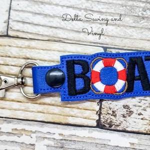 May include: Blue key chain with a black embroidered word "BOAT" and a red, white, and brown life preserver. The key chain has a silver metal clasp.