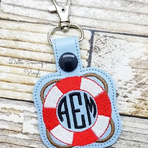 May include: A light blue key chain with a red, white, and brown embroidered life preserver with the monogram "AEM" in black thread.