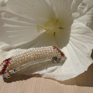 May include: A white pearl and burgundy red beaded hair clip with a silver metal clasp.